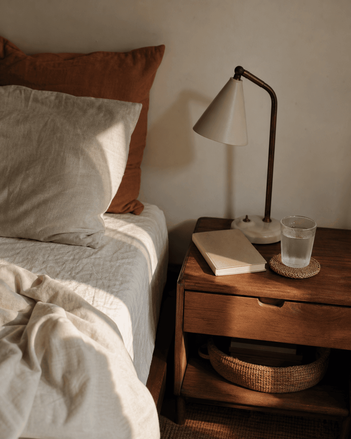 Linen bedding, a reading lamp, and a water glass by the bed