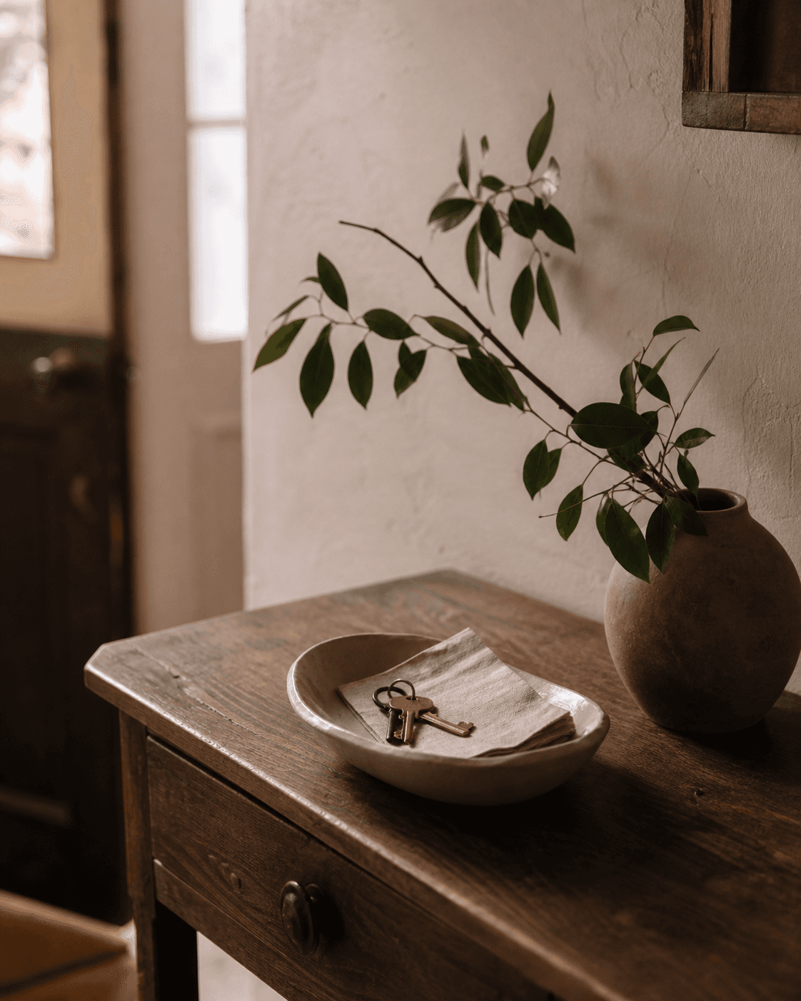 Keys and a linen note beside a leafy branch on an entry table